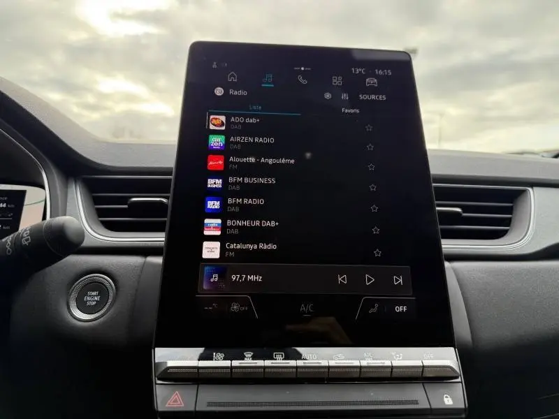 Vue intérieure centrée sur l'écran tactile du tableau de bord du Renault Captur 2025, avec commandes climatisation et bouton start/stop visible.