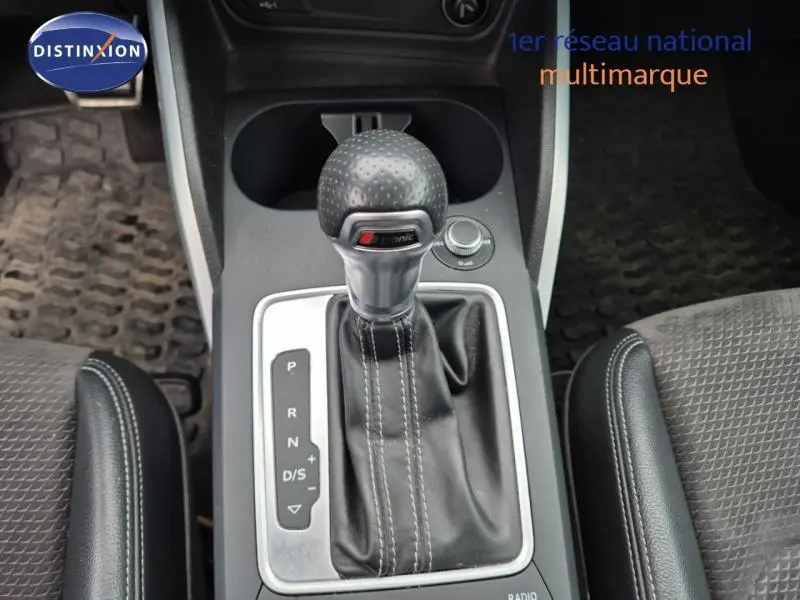 Vue rapprochée du levier de vitesses automatique S tronic noir avec surpiqûres blanches dans l'Audi Q2 gris Manhattan.
