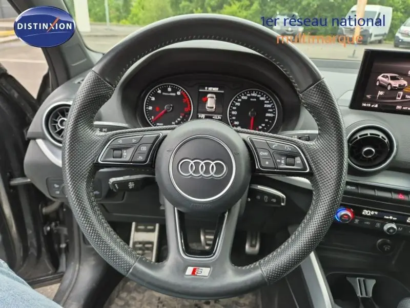 Vue intérieure centrée sur le volant sport en cuir perforé de l'Audi Q2 gris Manhattan avec tableau de bord et écran multifonction.