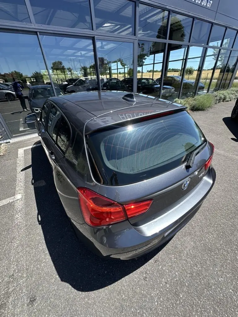 BMW Série 1 gris foncé vue en 3/4 arrière droit, soulignant les feux arrière et la lunette arrière teintée.