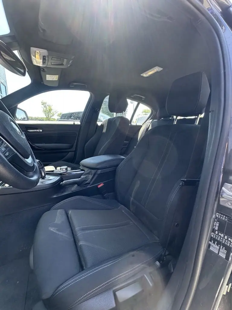 Intérieur avant côté conducteur d'une BMW Série 1 F20 gris foncé, sièges noirs avec surpiqûres blanches, console centrale visible.