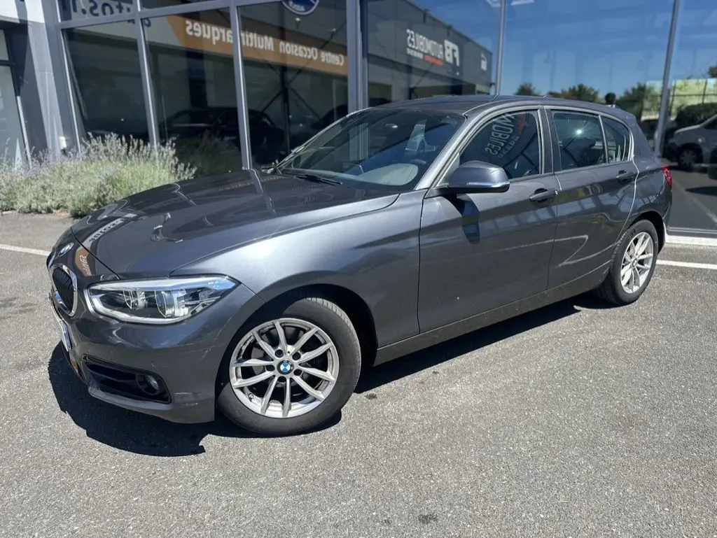 BMW Série 1 F20 gris foncé vue 3/4 avant côté gauche, avec jantes alliage et calandre caractéristique BMW.