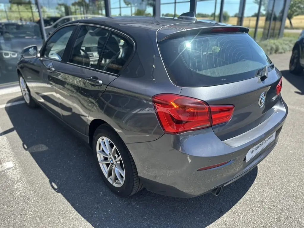 Vue 3/4 arrière droite d'une BMW Série 1 F20 gris foncé de 2019, avec feux arrière rouges et jantes alliage.