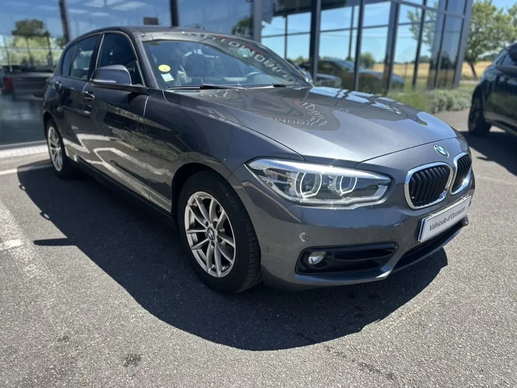 BMW Série 1 F20 gris foncé vue 3/4 avant droit, avec phares LED et calandre double haricot chromée.