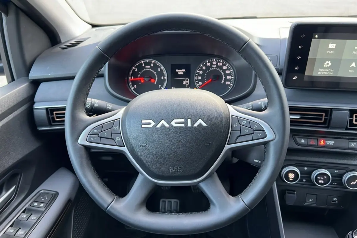 Vue intérieure centrée sur le volant DACIA d'une Sandero Stepway 2024, avec tableau de bord et écran tactile visibles.