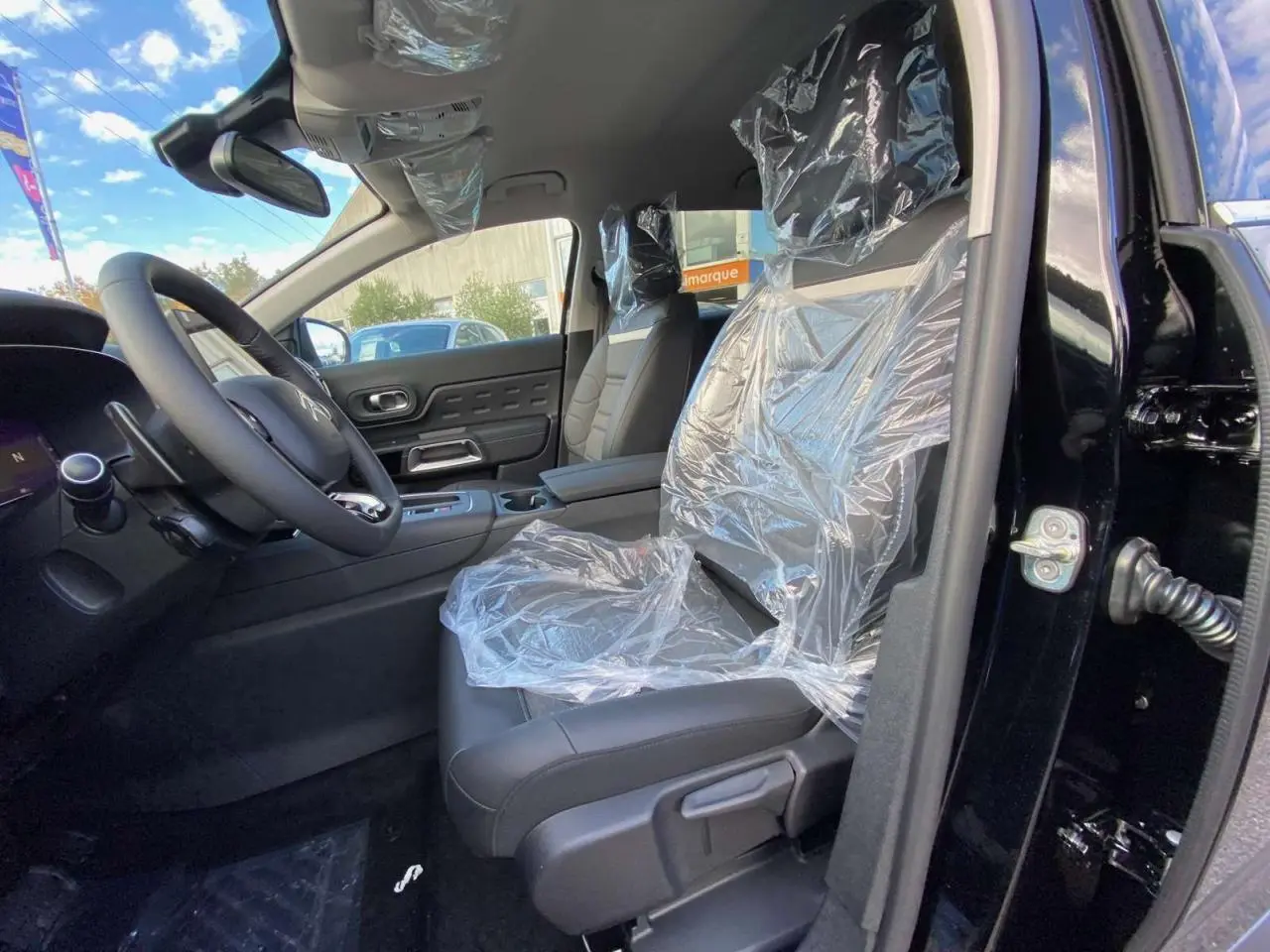 Intérieur avant droit du Citroën C5 Aircross noir Perla, sièges protégés par film plastique, volant et console visibles.