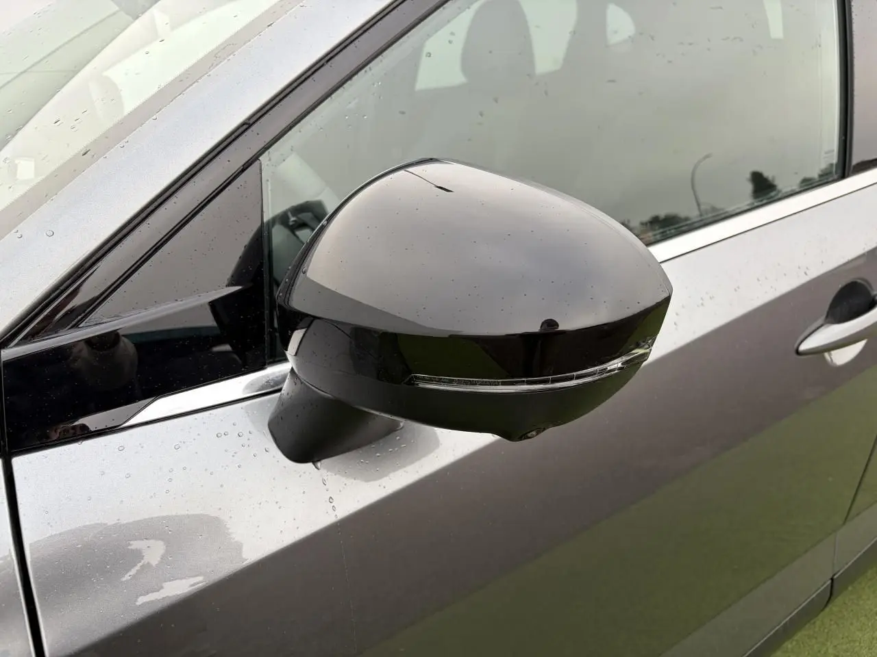 Gros plan sur le rétroviseur droit noir brillant du Nissan Qashqai III gris métallisé avec gouttes d'eau visibles.