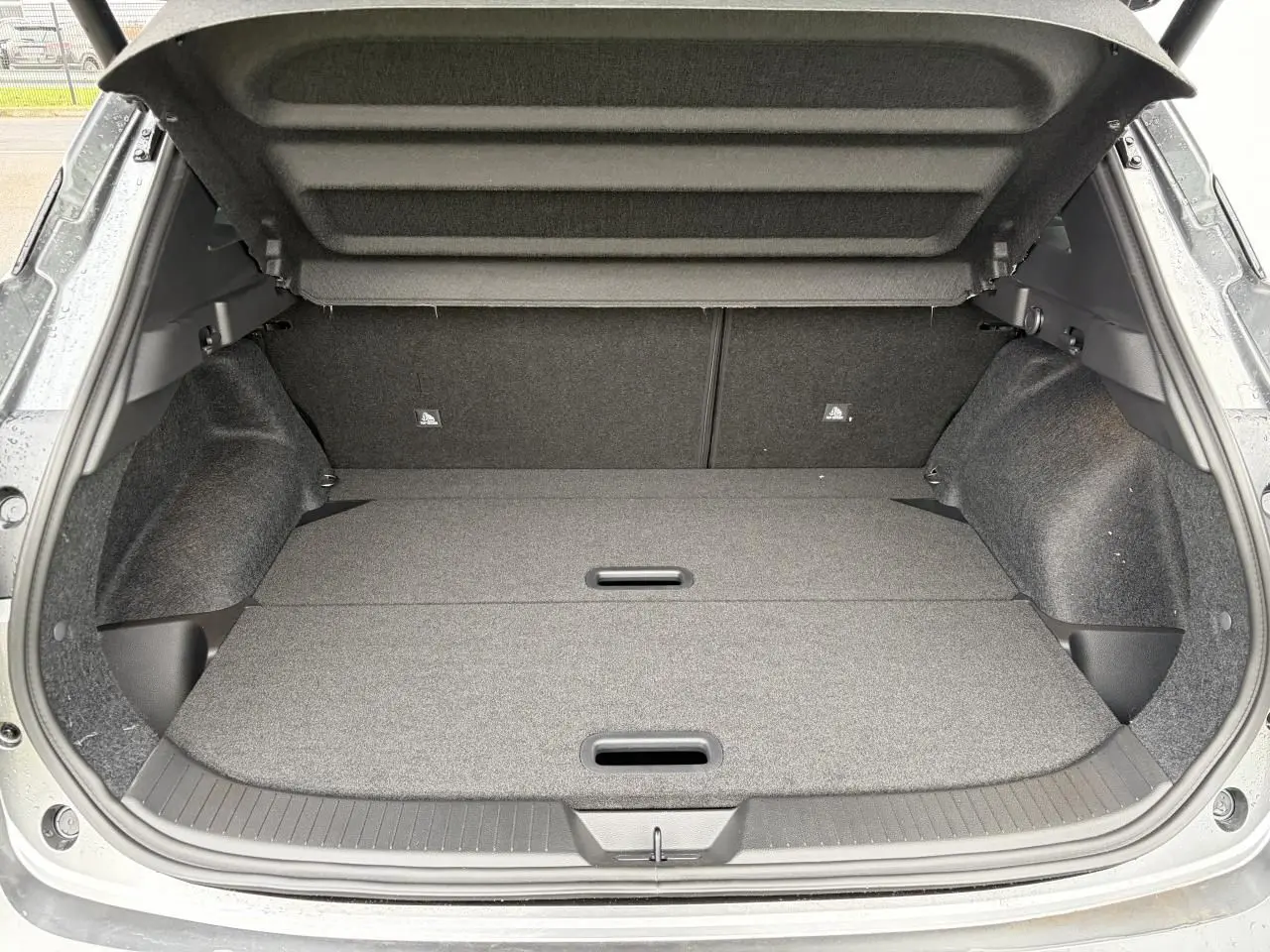 Coffre ouvert du Nissan Qashqai III 2025 gris foncé, vue arrière montrant un espace de chargement plat et doublé.