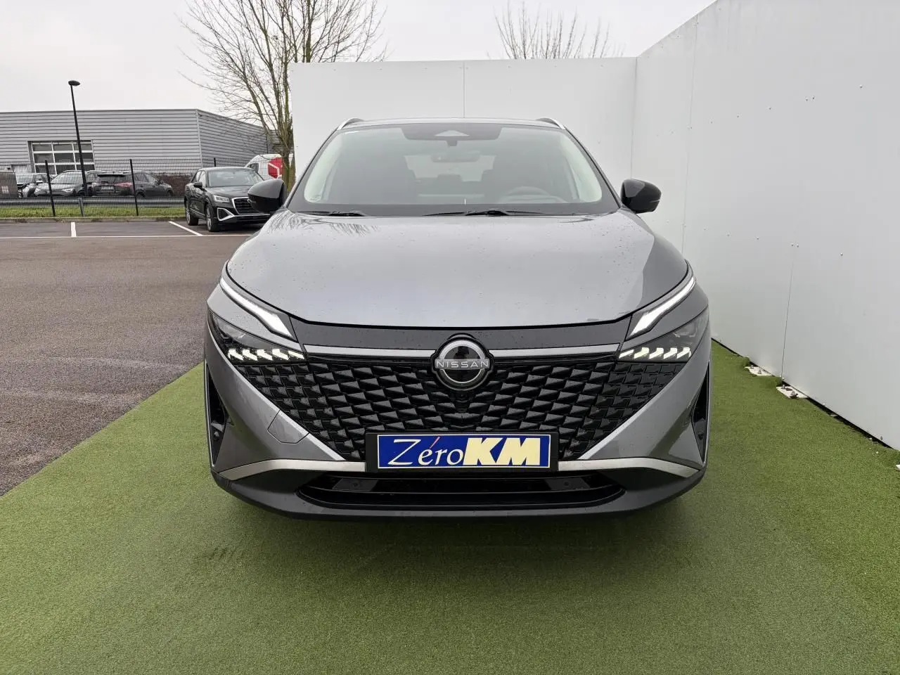 Vue frontale du Nissan Qashqai III 1.5 Hybrid E-Power gris foncé avec calandre noire et feux LED allumés.