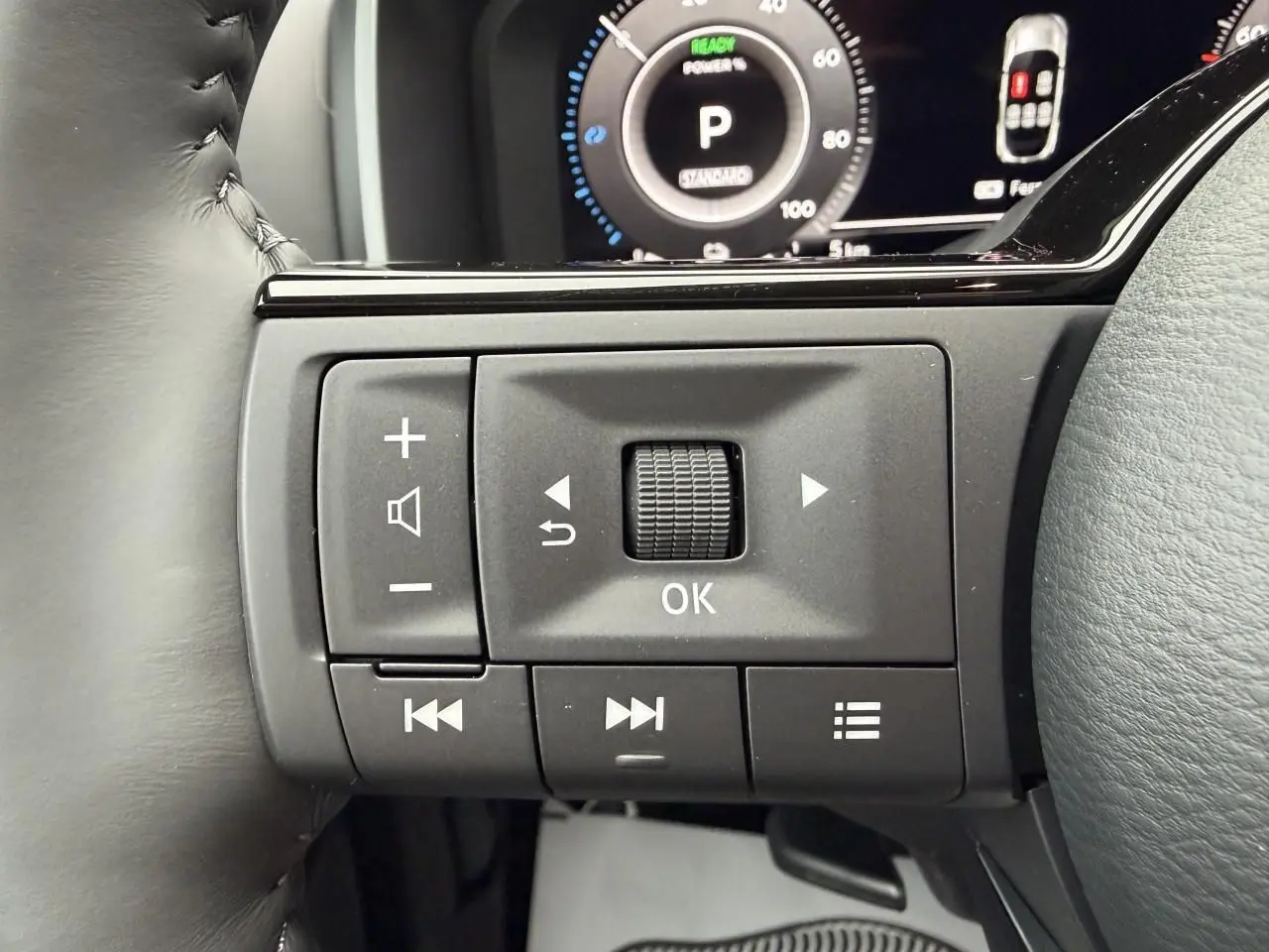 Gros plan sur les commandes multifonctions noires au volant du Nissan Qashqai III hybride, avec tableau de bord numérique en arrière-plan.