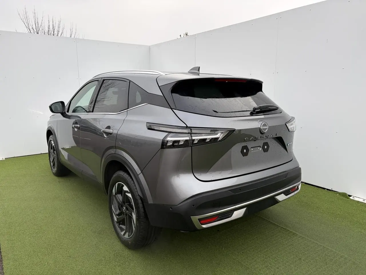 Vue 3/4 arrière droite du Nissan Qashqai 2025 gris foncé métallisé avec feux LED et barres de toit chromées.
