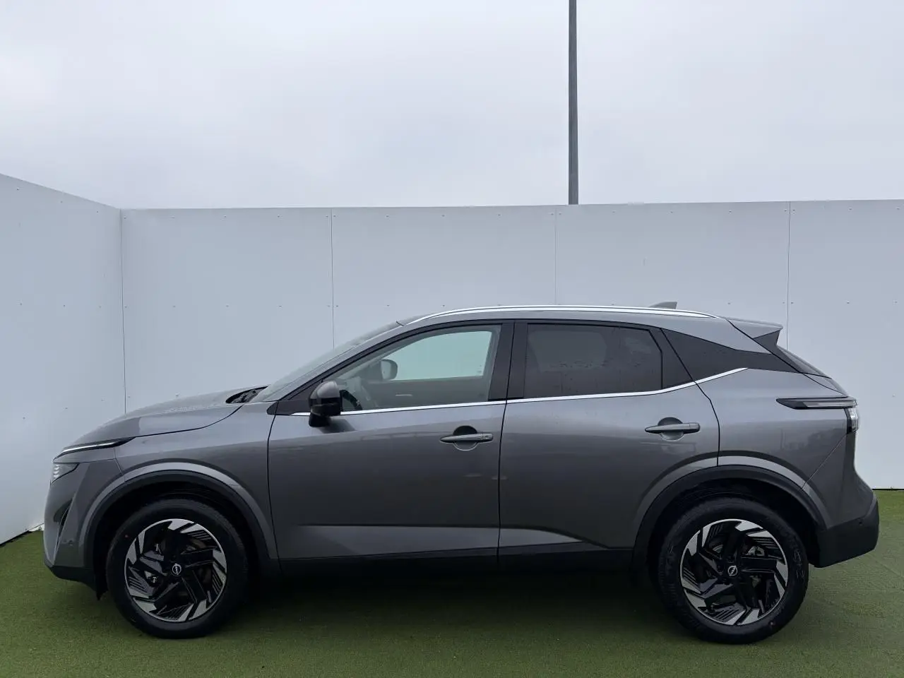 Profil droit du Nissan Qashqai III 1.5 Hybrid E-Power 2025 en gris métallisé avec jantes alliage noires et toit contrasté.