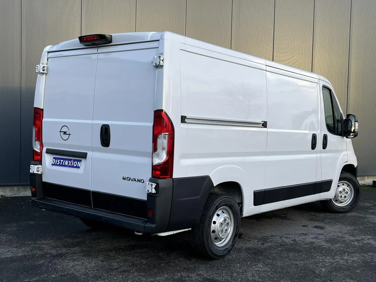 Vue 3/4 arrière droite d'un fourgon Opel Movano blanc avec portes arrière battantes et protections noires sur bas de caisse.