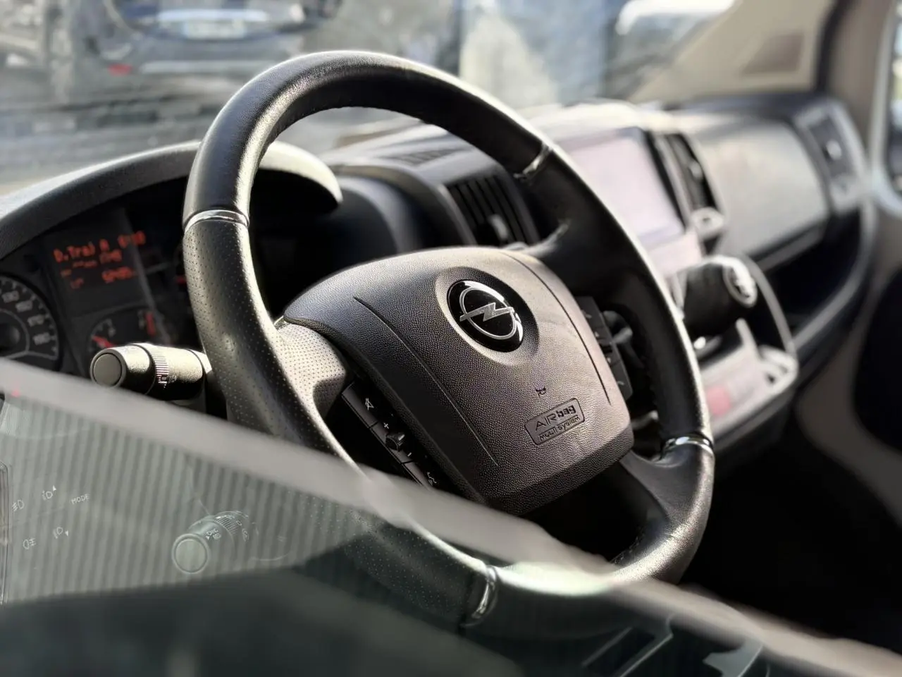 Gros plan sur le volant noir de l'Opel Movano Fourgon 2024, avec tableau de bord et écran tactile en arrière-plan.