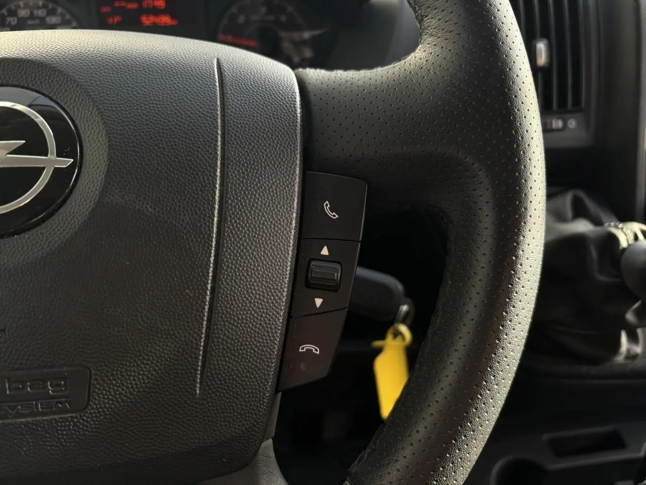 Gros plan sur le volant noir perforé d’un Opel Movano 2024 avec commandes d’appel et levier de vitesse manuel visible.