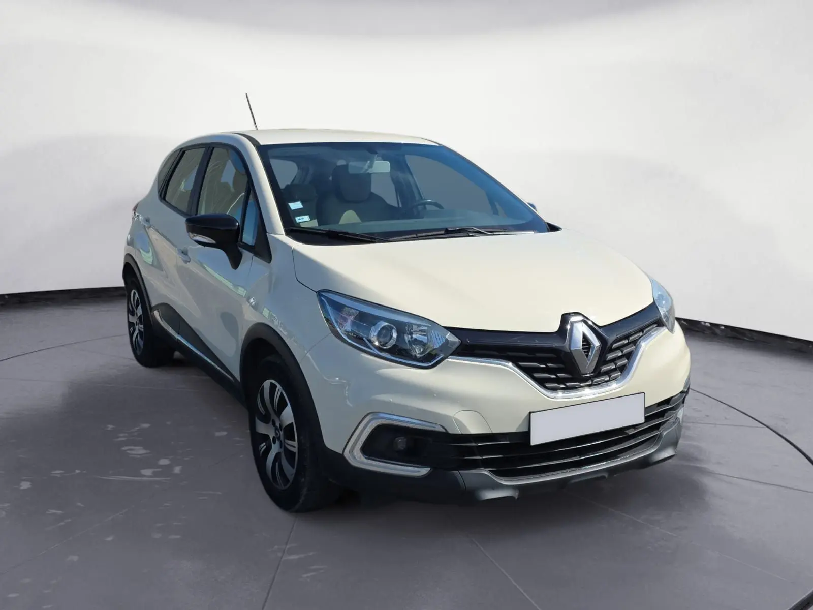 Renault Captur ivoire vue 3/4 avant droit, mettant en valeur ses optiques modernes et sa calandre chromée distinctive.