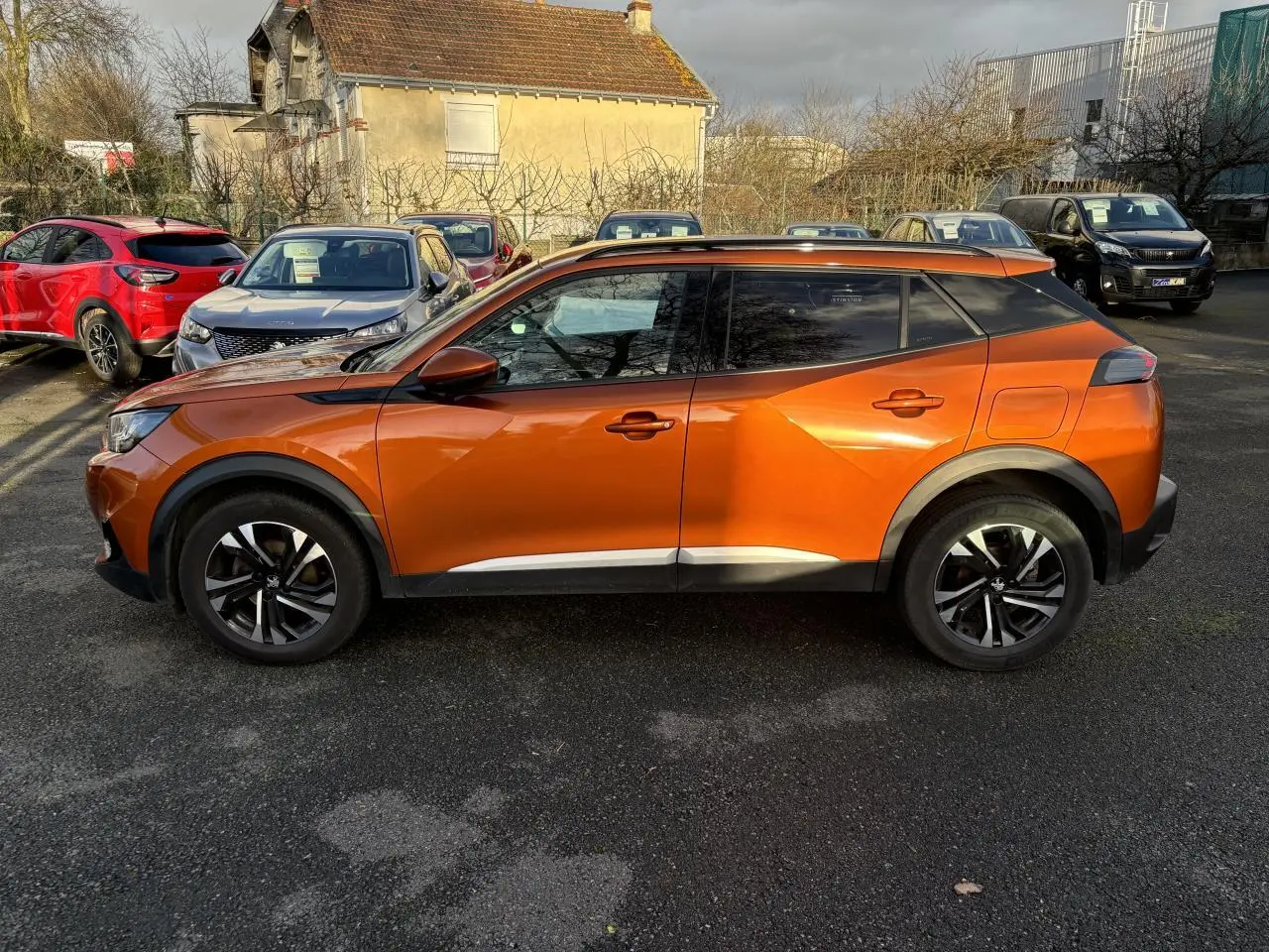 Vue de profil côté gauche d'un Peugeot 2008 2021 orange fusion avec jantes alliage et vitres teintées.