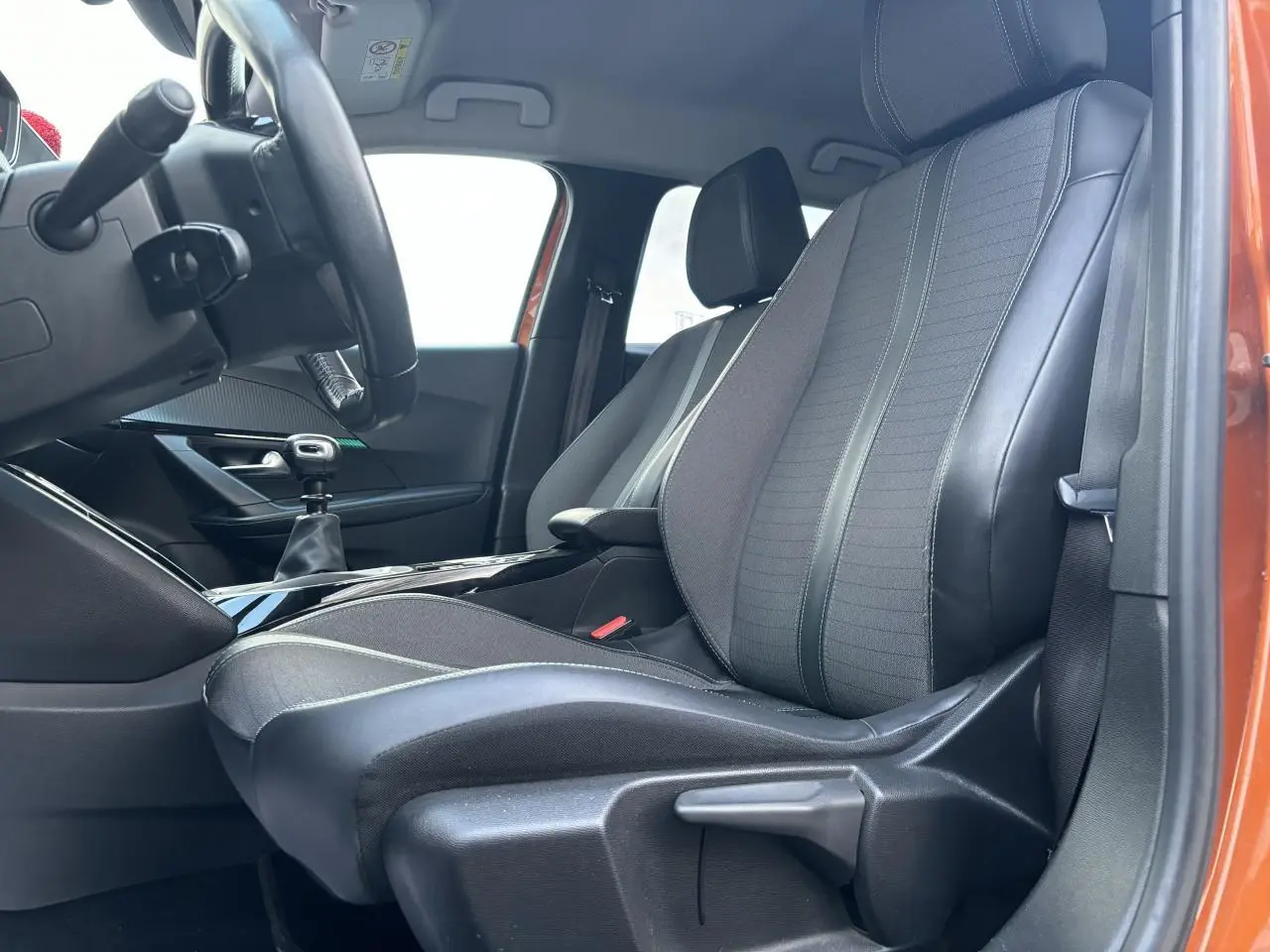 Vue intérieure côté conducteur du Peugeot 2008 2021 Orange Fusion, sièges tissu et cuir avec levier de vitesse manuel visible.