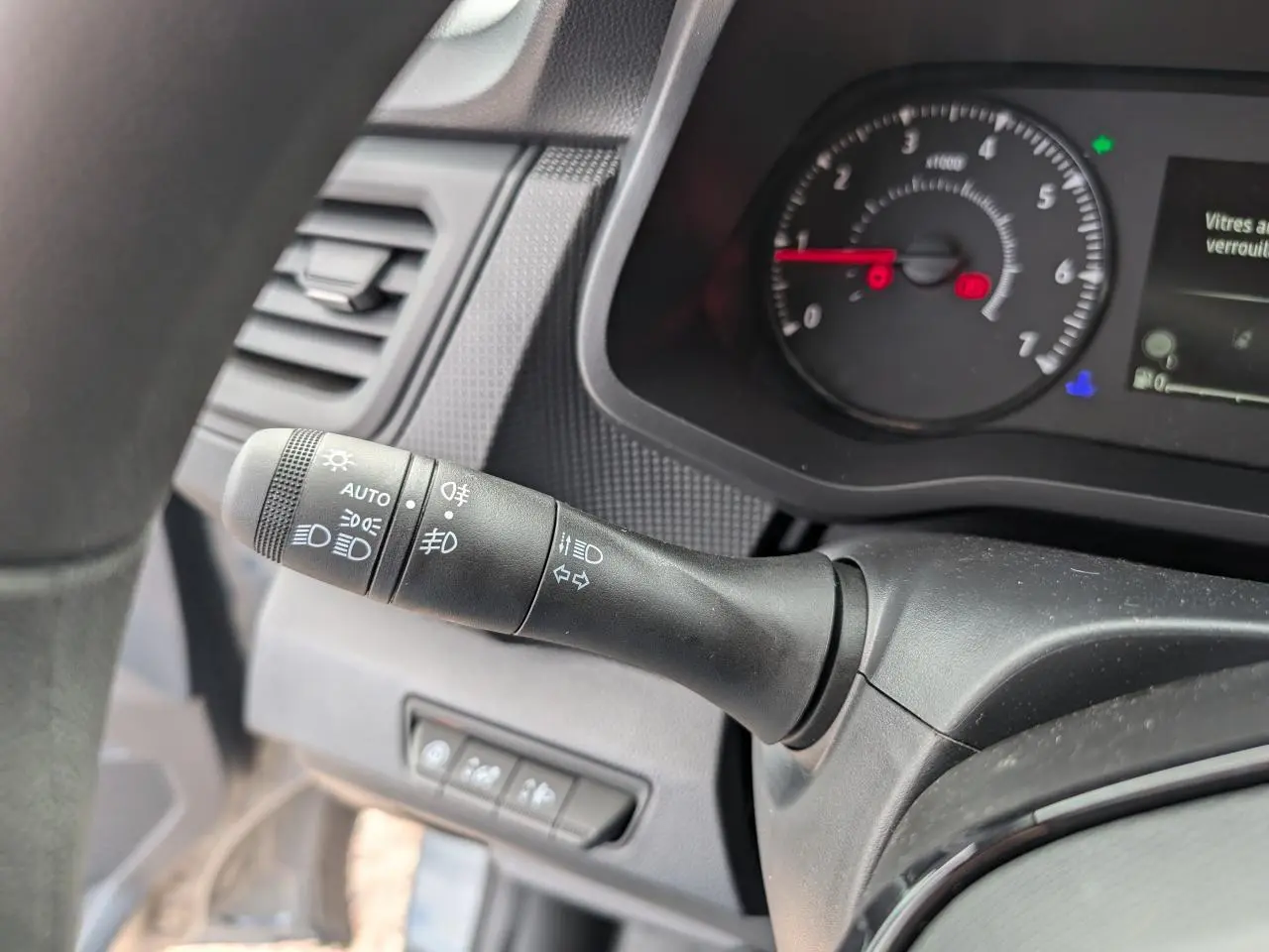 Gros plan sur la commande des phares et clignotants à gauche du tableau de bord du Renault Trafic Fourgon gris 2024.