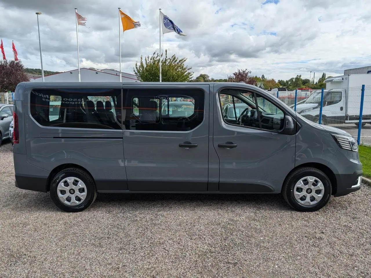 Profil latéral droit d'un Renault Trafic Fourgon gris Urban 2024 avec vitres teintées et jantes enjoliveurs 16 pouces.