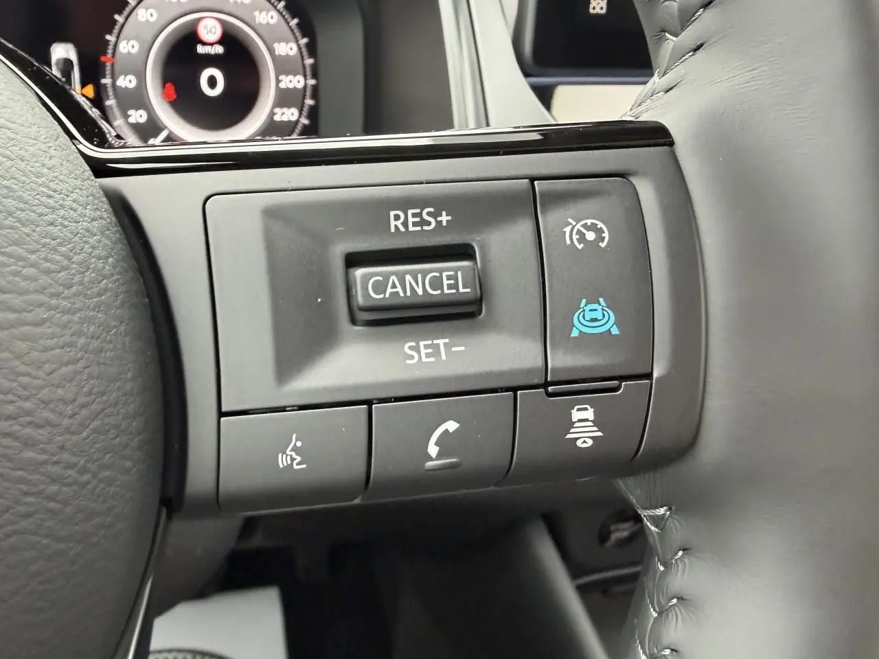 Gros plan sur les commandes au volant du Nissan Qashqai III hybride, avec affichage numérique partiel en arrière-plan.