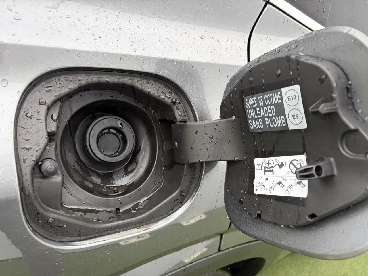 Gros plan sur la trappe à carburant ouverte du Nissan Qashqai 2025 gris foncé, avec étiquette essence sans plomb visible.
