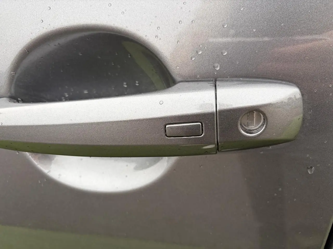 Poignée de porte avant droite gris métallisé du Nissan Qashqai 2025 avec bouton d'ouverture mains libres sous pluie.