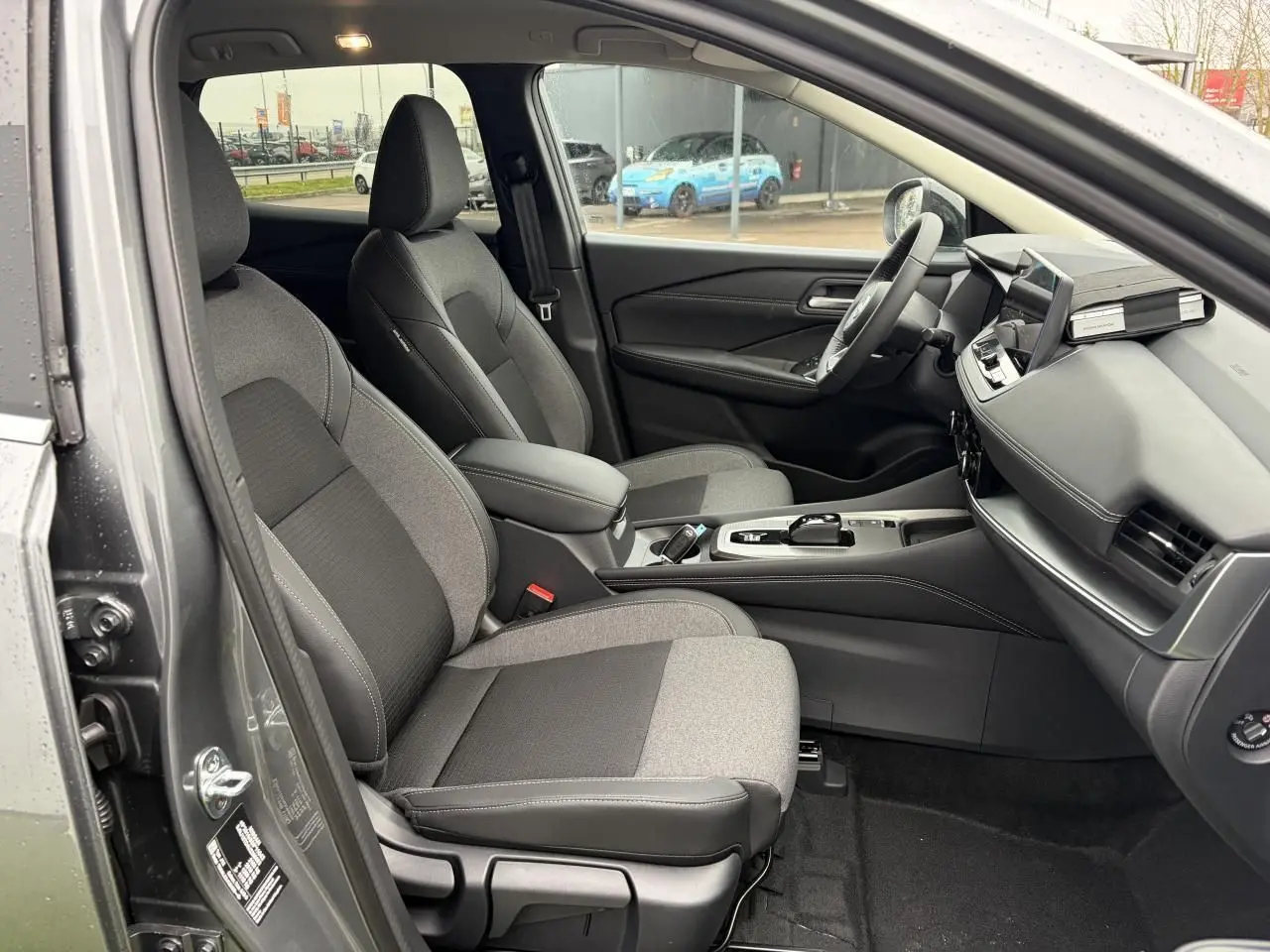 Vue intérieure côté gauche du Nissan Qashqai 2025 gris foncé, montrant sièges tissu et tableau de bord moderne.