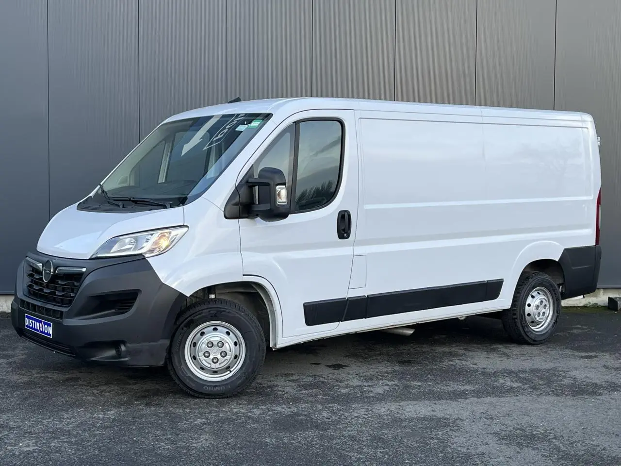 Vue 3/4 avant droit d’un Opel Movano Fourgon blanc 2024 avec pare-chocs noirs et porte latérale coulissante.