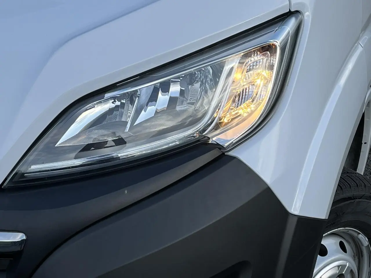 Gros plan sur le phare avant droit du fourgon blanc Opel Movano 2024, avec clignotant allumé et pare-chocs noir.