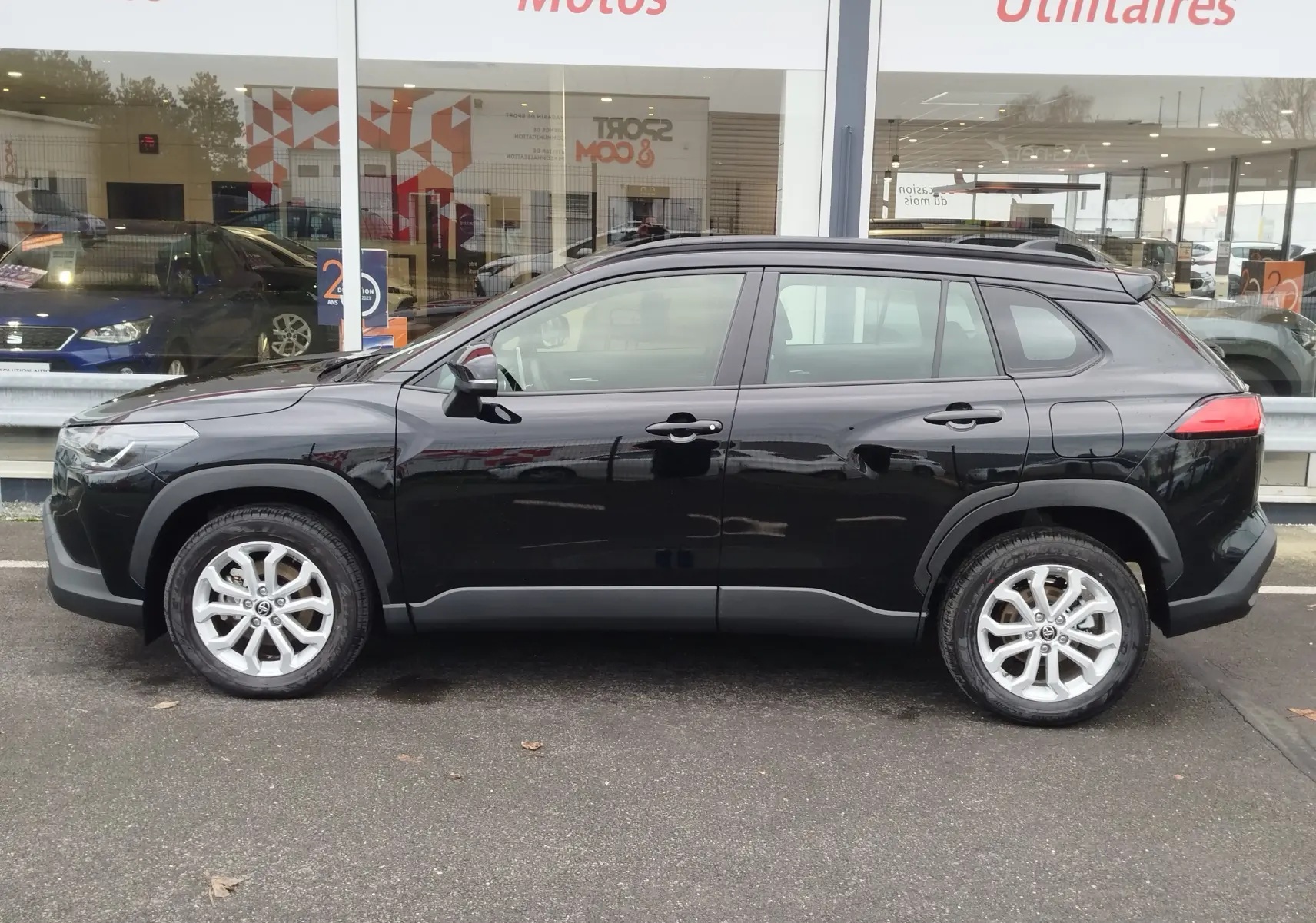 Vue de profil côté gauche d’un Toyota Corolla Cross 1.8 hybride noir intense, avec jantes alliage et protections noires.