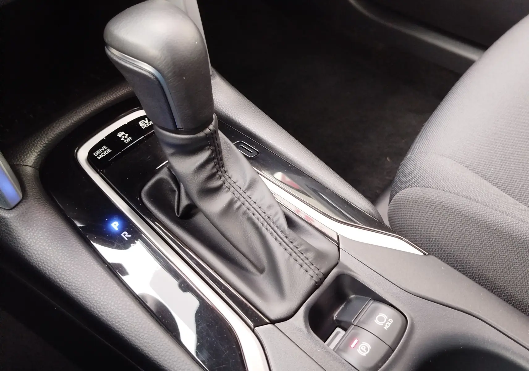 Gros plan sur la console centrale de la Toyota Corolla Cross 2025, levier de vitesse automatique en cuir noir et commandes électroniques.