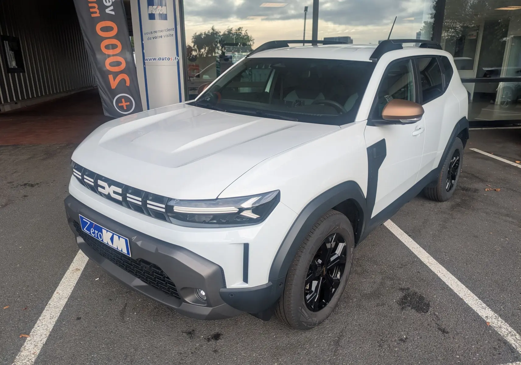 Vue 3/4 avant droite du Dacia Duster Hybrid 155 Extreme blanc glacier avec coques de rétroviseurs brun cuivré et jantes noires 17 pouces.