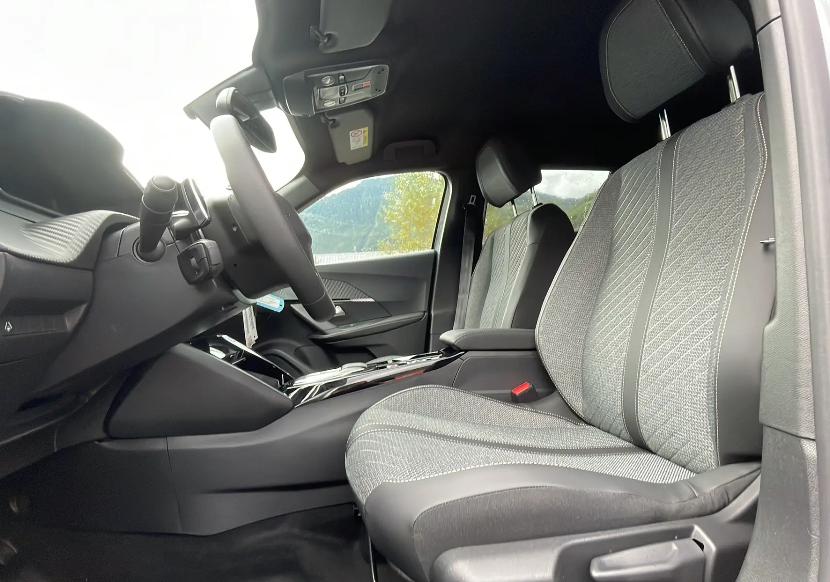 Intérieur du Peugeot 2008 2024, vue côté conducteur, sièges tissu gris avec surpiqûres et console centrale moderne.