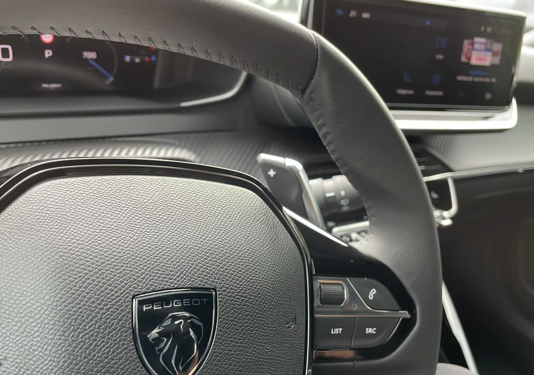 Vue rapprochée du volant cuir noir avec logo Peugeot et tableau de bord numérique du 2008 Gris Artense 2024.
