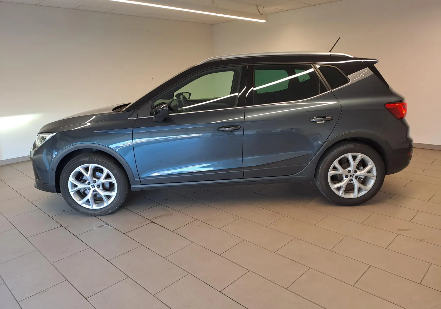 Vue de profil côté gauche du SEAT Arona 1.0 TSI 110 DSG7 FR 2024 en gris magnétique avec toit noir et jantes 18 pouces.