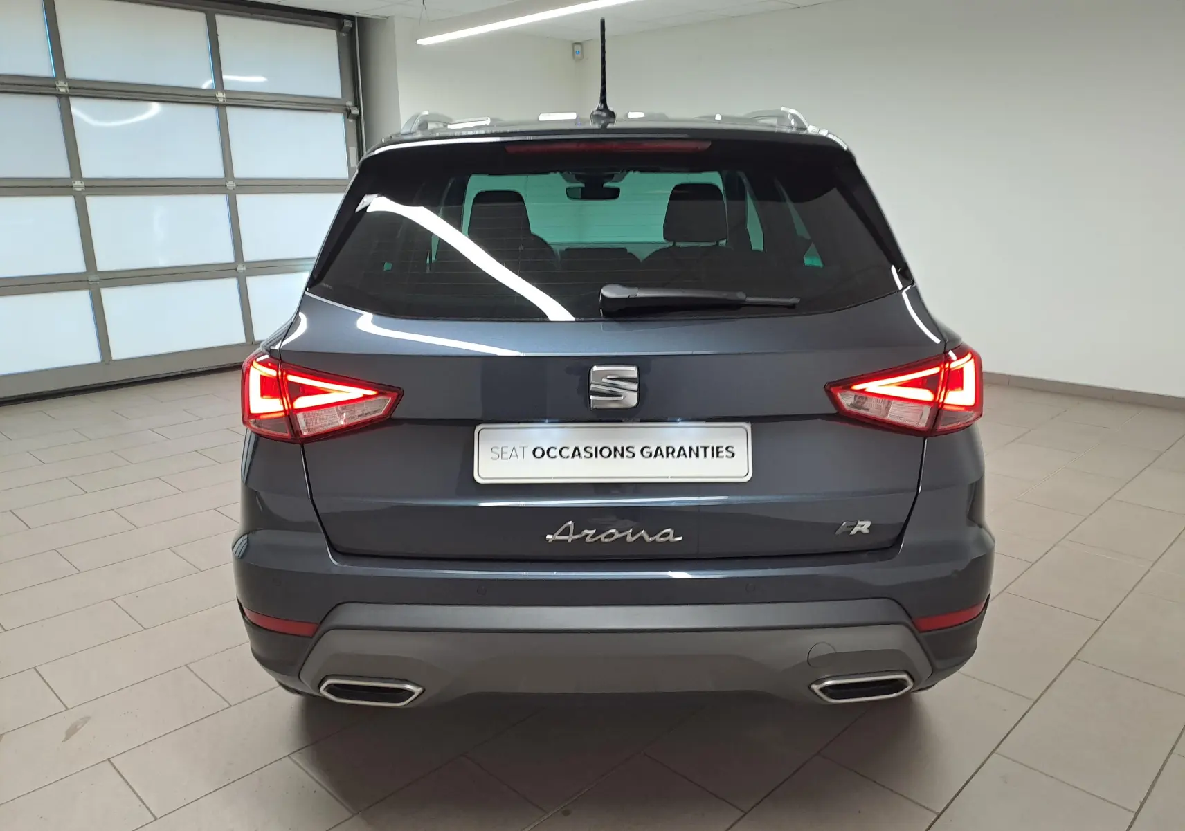 Vue arrière d'un SEAT Arona 2024 gris magnétique avec toit noir et feux arrière allumés en intérieur.