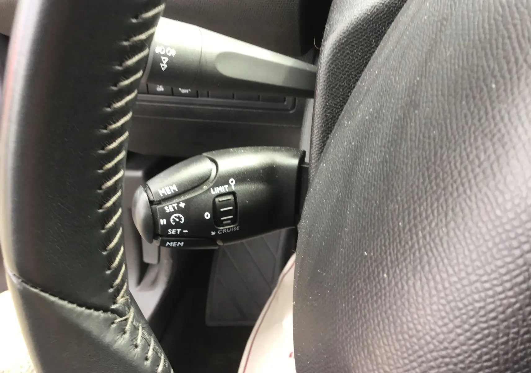 Gros plan sur le commodo de régulateur de vitesse à gauche du volant en cuir noir de la Peugeot 308 gris Artense.