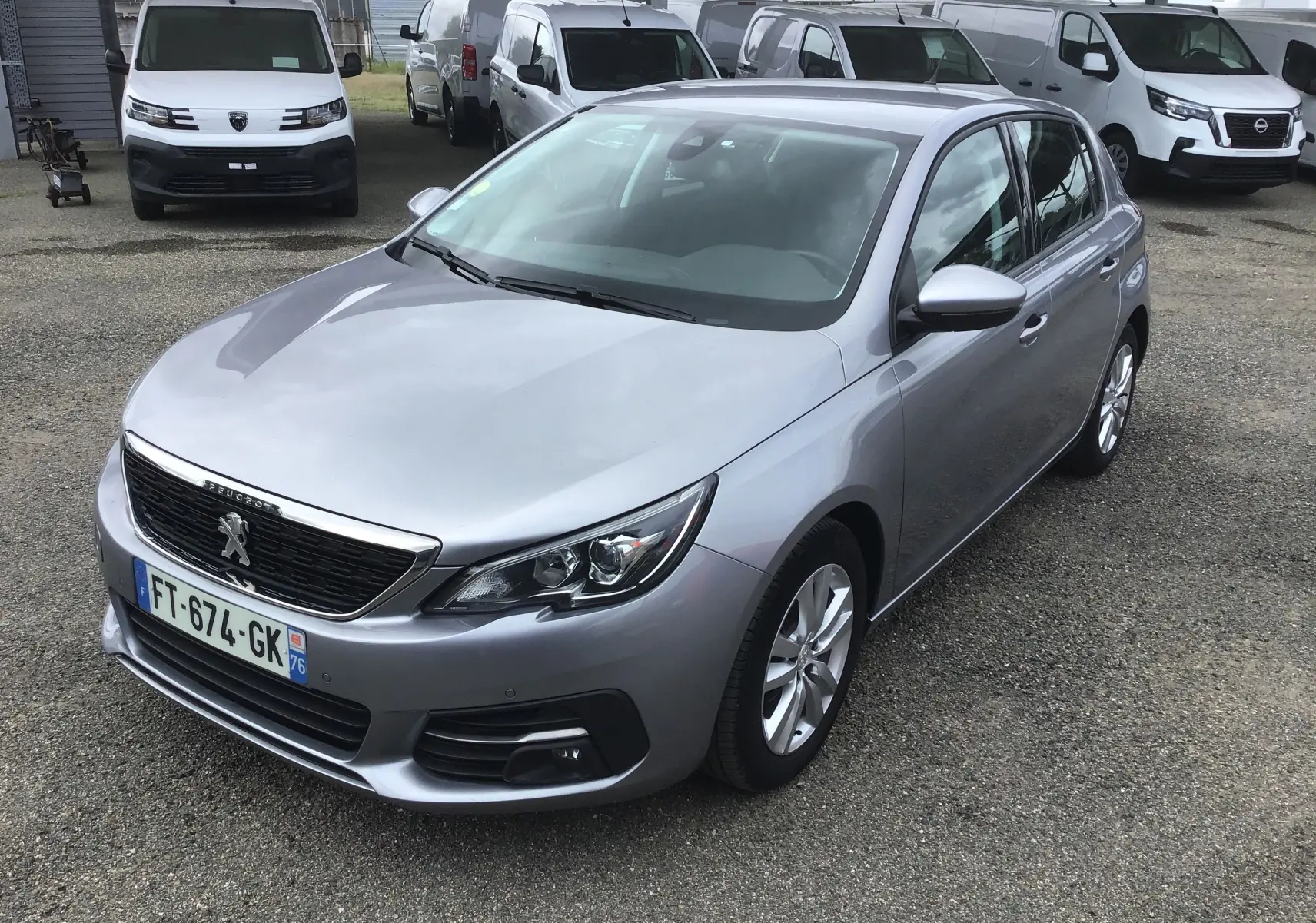 Vue 3/4 avant droite d'une Peugeot 308 gris Artense de 2020, avec calandre noire et jantes alliage argentées.