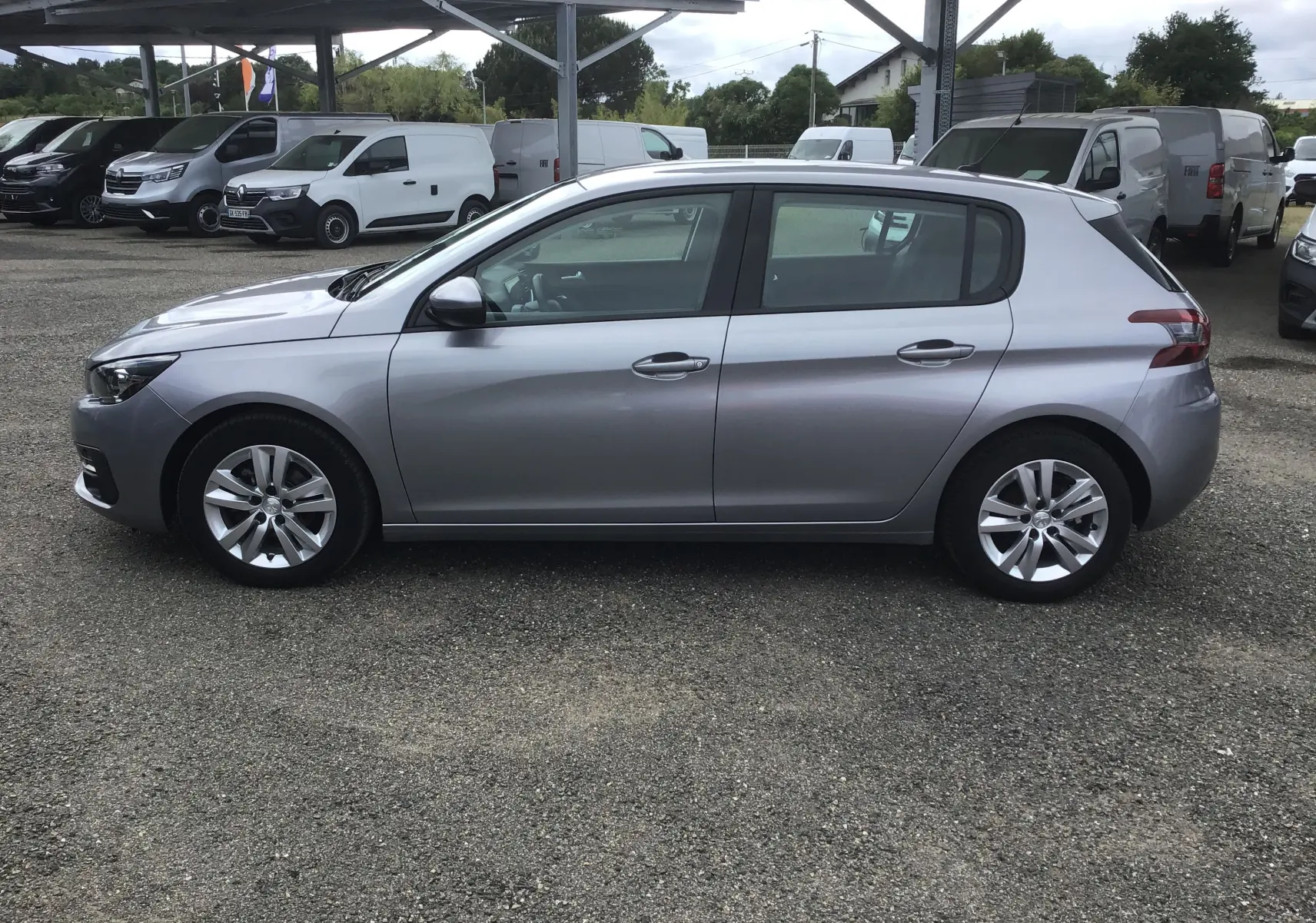 Vue de profil côté gauche d'une Peugeot 308 gris artense 2020 garée sur un parking extérieur sous un abri.