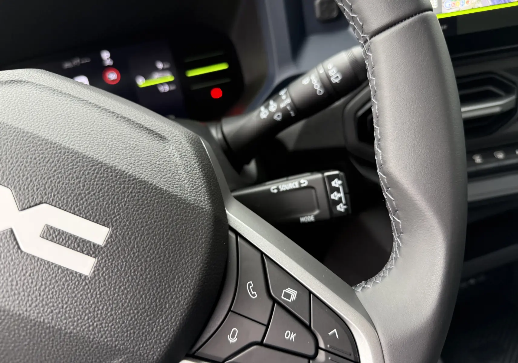 Gros plan sur le volant gris du Dacia Duster 2025 avec commandes intégrées et tableau de bord numérique en arrière-plan.