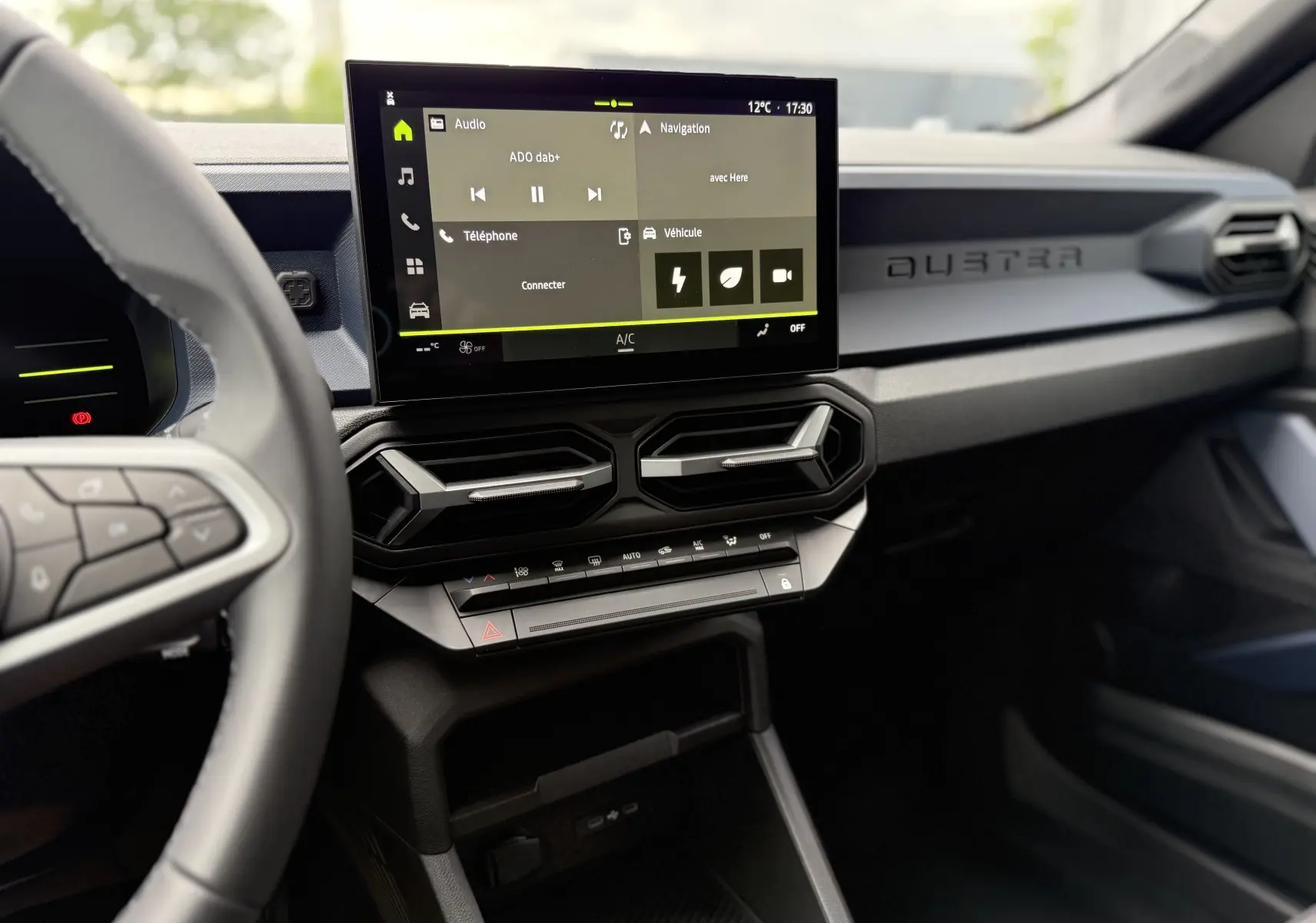 Vue intérieure du tableau de bord du Dacia Duster 2025 gris schiste, avec écran tactile central et commandes climatisation.