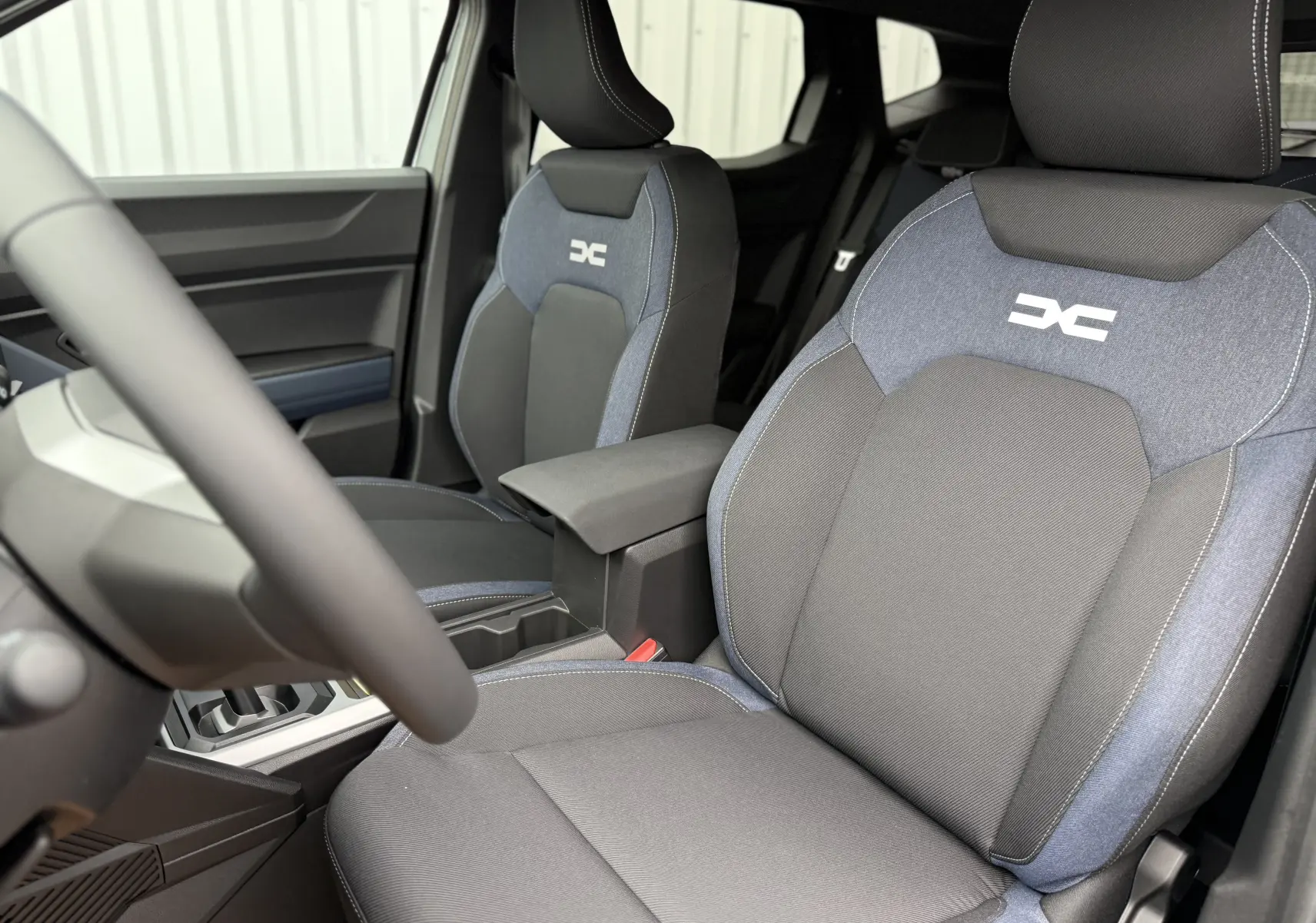 Vue intérieure du Dacia Duster 2025 montrant les sièges avant en tissu gris et bleu avec logo distinctif brodé.