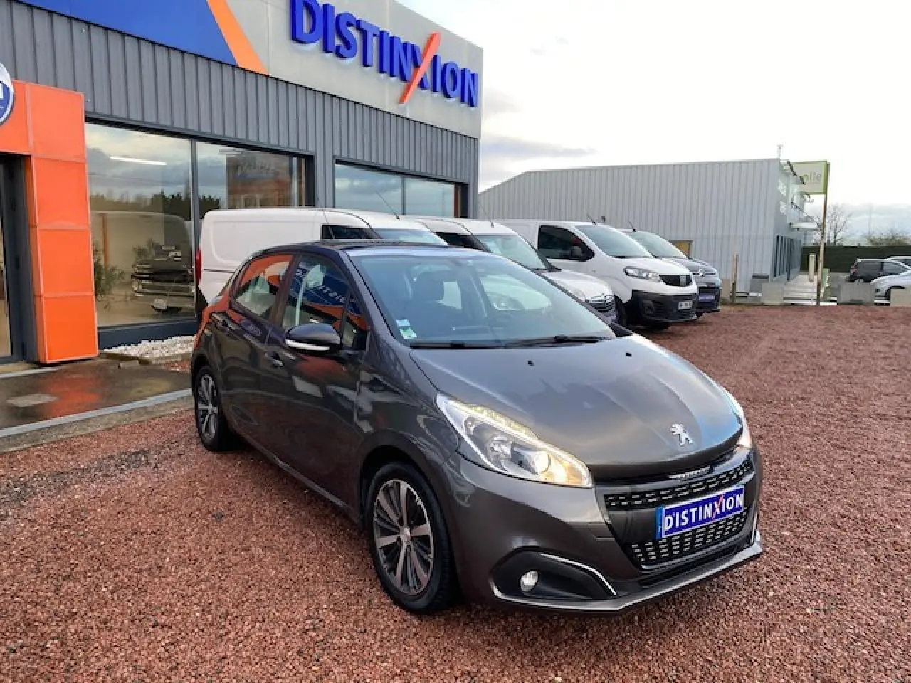 PEUGEOT 208 gris métallisé vue 3/4 avant droit, avec phares allumés et jantes alliage 16 pouces titane.