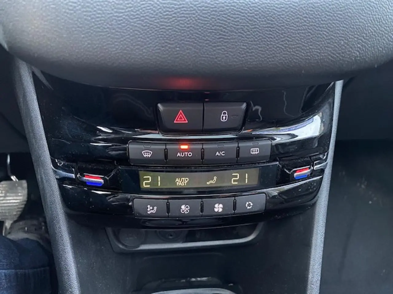 Gros plan sur la console centrale noire brillante de la Peugeot 208 gris, affichant la climatisation automatique à 21°C.