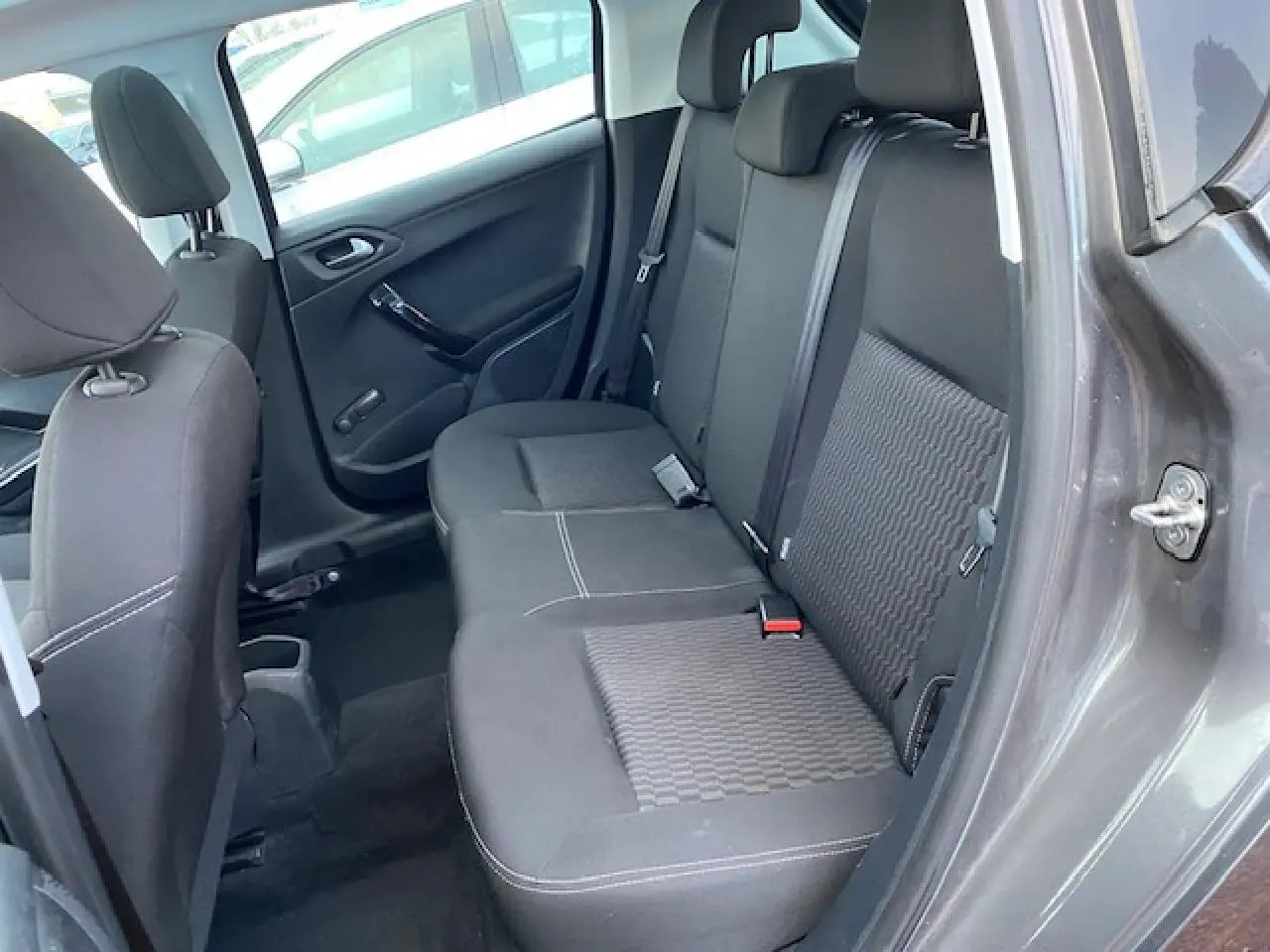 Vue côté droit de l'habitacle arrière d'une Peugeot 208 gris métallisé avec sièges tissu noir et ceinture de sécurité.