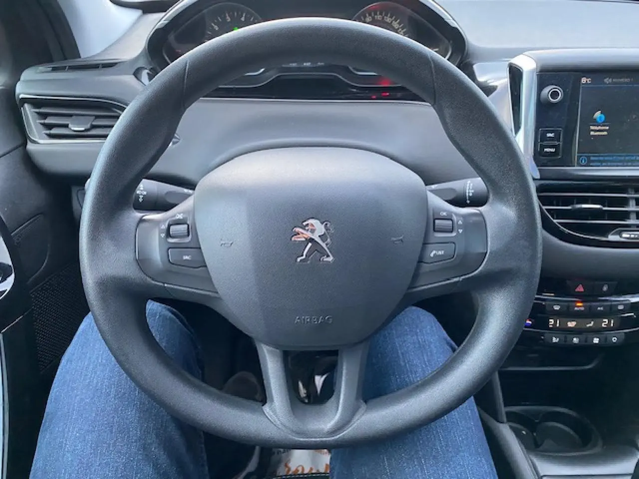 Vue rapprochée du volant multifonction noir d'une Peugeot 208 gris, avec tableau de bord et écran tactile visible.