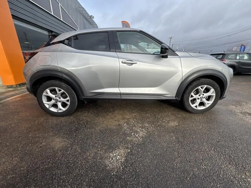 Vue de profil côté gauche d'un Nissan Juke gris perle métallisé avec jantes alliage, garé devant un bâtiment.