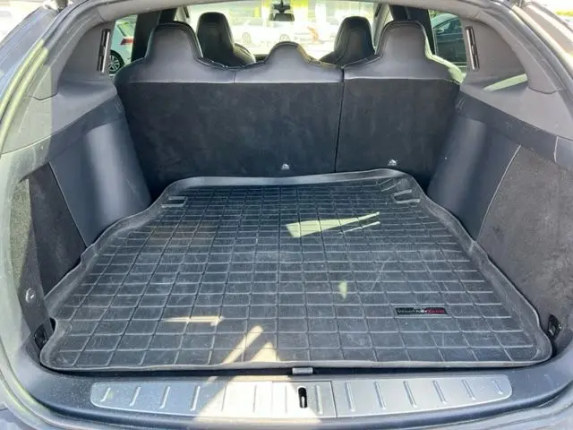 Vue depuis l'arrière du coffre ouvert d'un Tesla Model X gris 2019, avec tapis de protection noir et sièges arrière visibles.