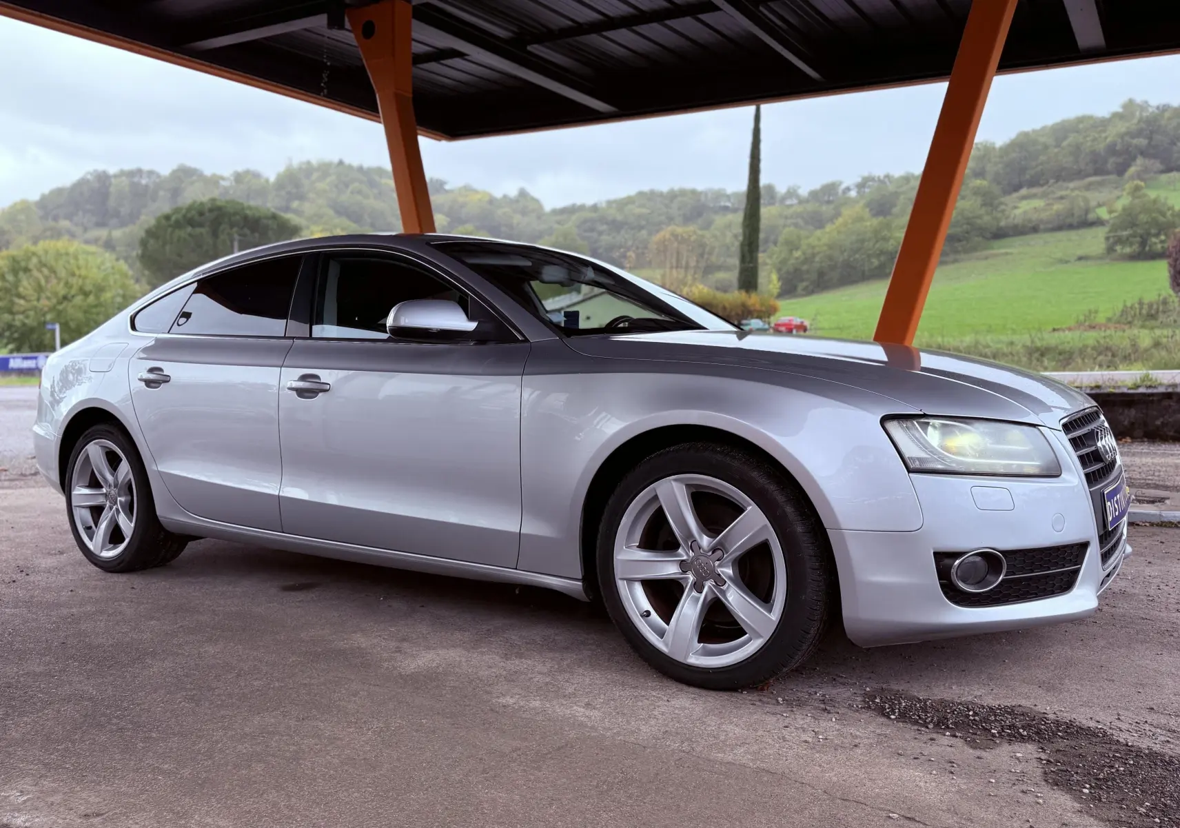 Audi A5 gris vue 3/4 avant droit sous un abri, avec jantes alliage et vitres teintées.